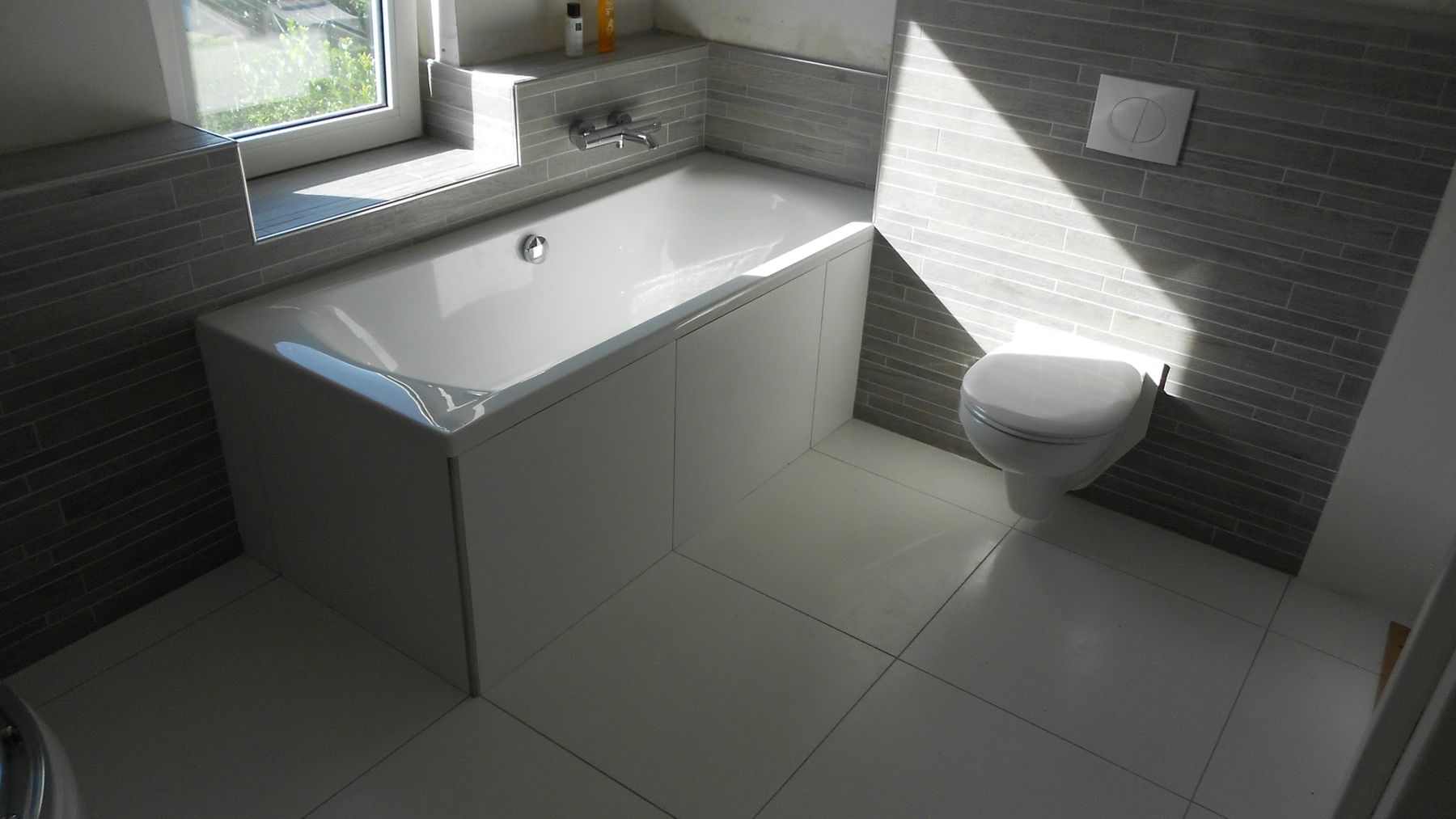 Getegelde badkamer met ligbad, hangtoilet en grijze natuursteenlook wandtegels