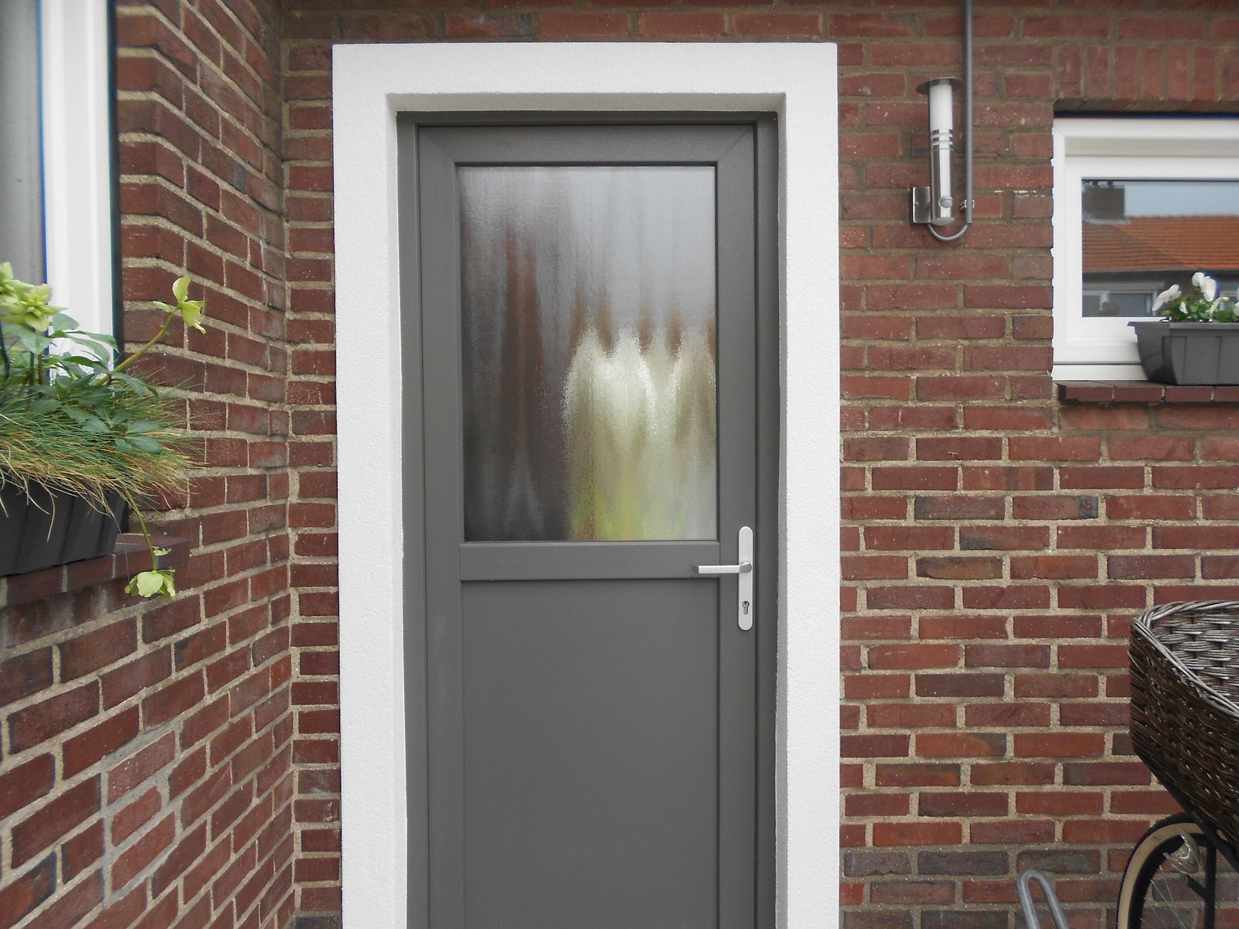 Nieuwe antraciet buitendeur met matglas geplaatst in een bakstenen muur