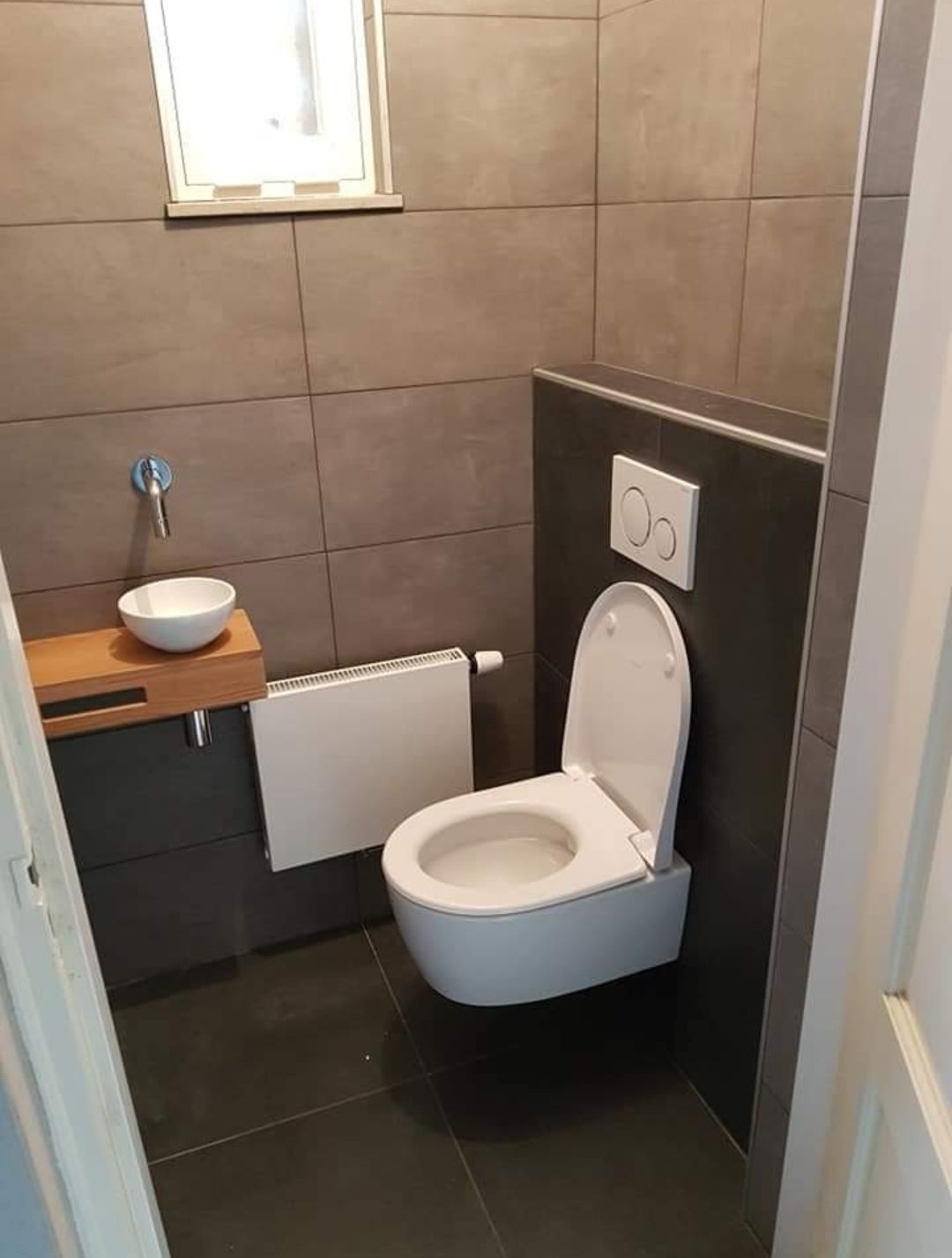 Toiletruimte met grote donkere tegels, hangtoilet en houten wastafelmeubel